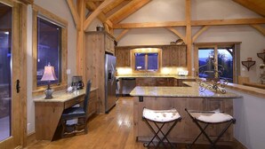 A kitchen with wooden beams, a central island, bar stools, and a window overlooking a scenic view. - Chateau Renard (Crested Butte)