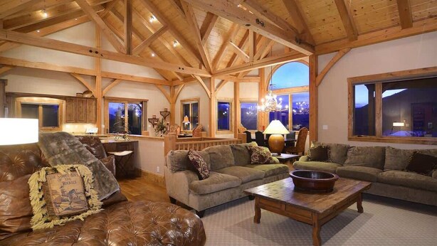 A spacious living area with a high wooden ceiling, leather sofas, a wooden coffee table, and large windows offering a view. - Chateau Renard (Crested Butte)