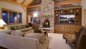 A cozy living room with a stone fireplace, wooden beams, a large window, and a leather armchair. - Chateau Renard (Crested Butte)