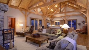 A spacious living area with a high wooden ceiling, a fireplace, a sofa, a coffee table, and a kitchen in the background. - Chateau Renard (Crested Butte)