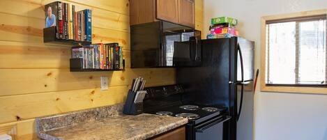 A compact kitchen with wooden cabinets, a granite countertop, a black stove, a microwave, and a refrigerator.