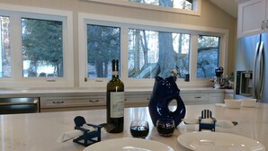 A modern kitchen with large windows, a wine bottle, and two plates on the counter. - Lake Rosseau - Rare, Flat double lot with breathtaking South West views. (Minett)