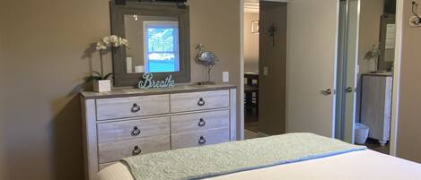 A bedroom with a bed, dresser, ceiling fan, and a TV mounted on the wall.