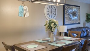 Een eetruimte met een houten tafel, comfortabele stoelen, een kroonluchter, een wandklok en decoratieve muurkunst.