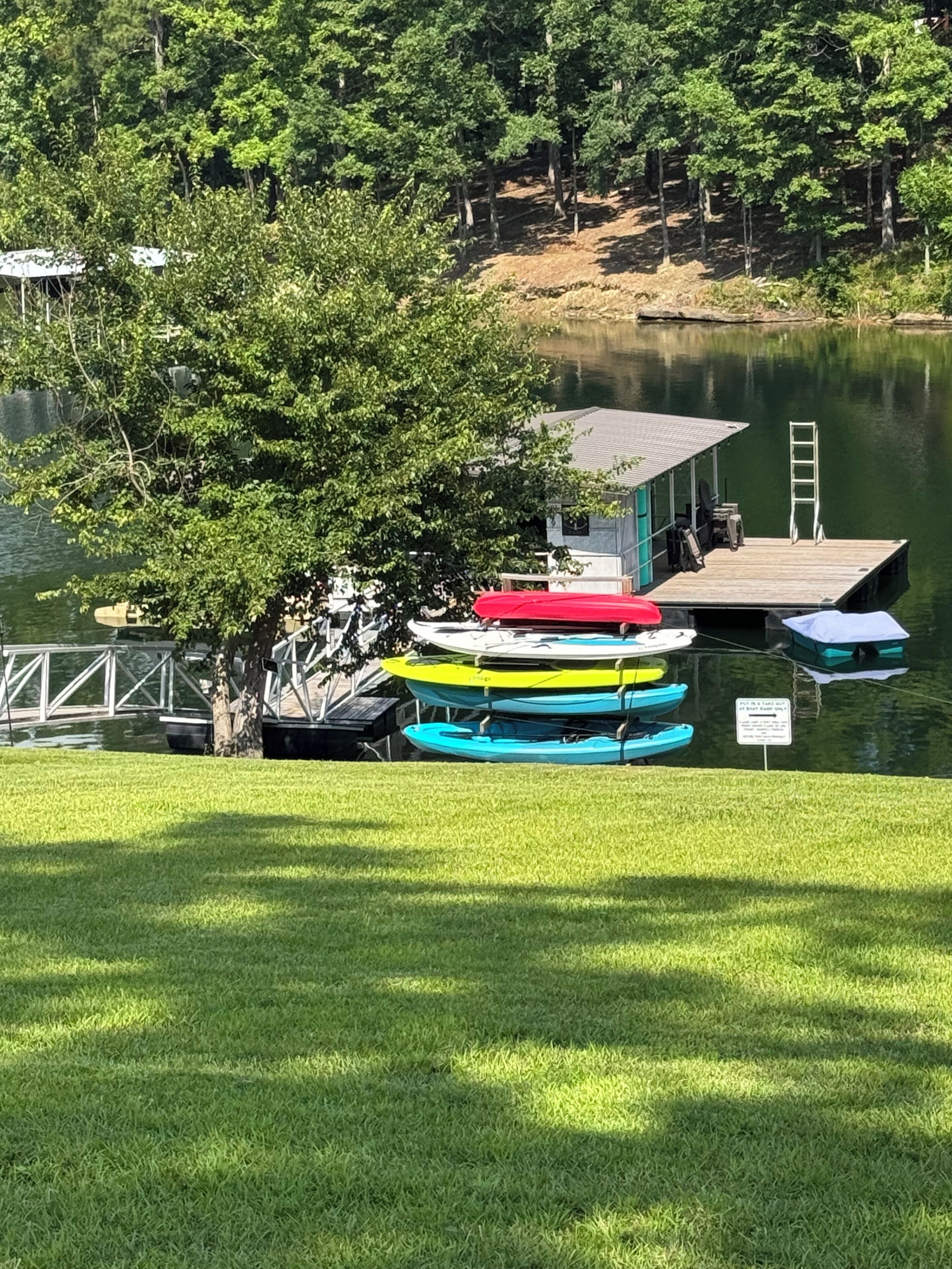 Ein Steg mit Booten, ein überdachter Bereich und eine Wiese am See.