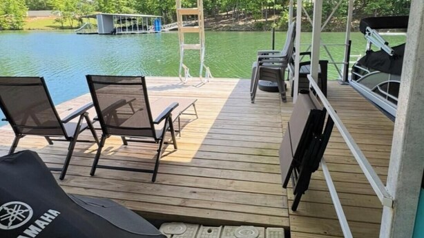 Een overdekt terras met uitzicht op een meer, zitplaatsen buiten en een Yamaha barbecue.