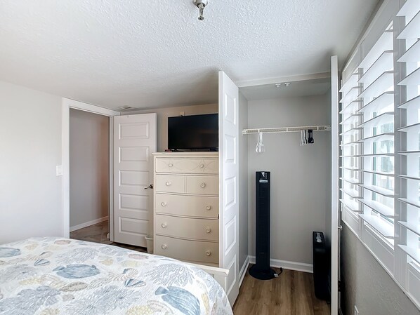 Un dormitorio con cama, cómoda, televisor y ventilador.