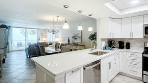 Una cocina moderna con armarios blancos, una isla grande con un fregadero y un comedor con una araña.