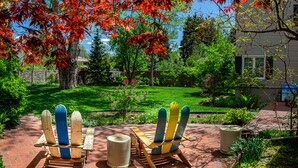 A patio with two Adirondack chairs, a brick pathway, and a grassy yard with trees. - The Best VRBO In Colorado Springs.  Our Reviews Prove It.  Near All The Venues  (Colorado Springs)