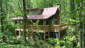 Une cabane à deux étages dotée d’un balcon, entourée d’une forêt dense.