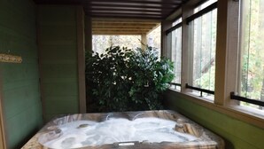 Un bain à remous avec une structure extérieure en bois, entouré d’une terrasse en bois et d’un mur végétal.