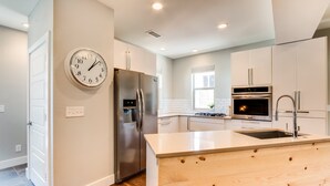 A modern kitchen with a central island, stainless steel appliances, and a wall clock. - Downtown Views and Brews (Fort Collins)