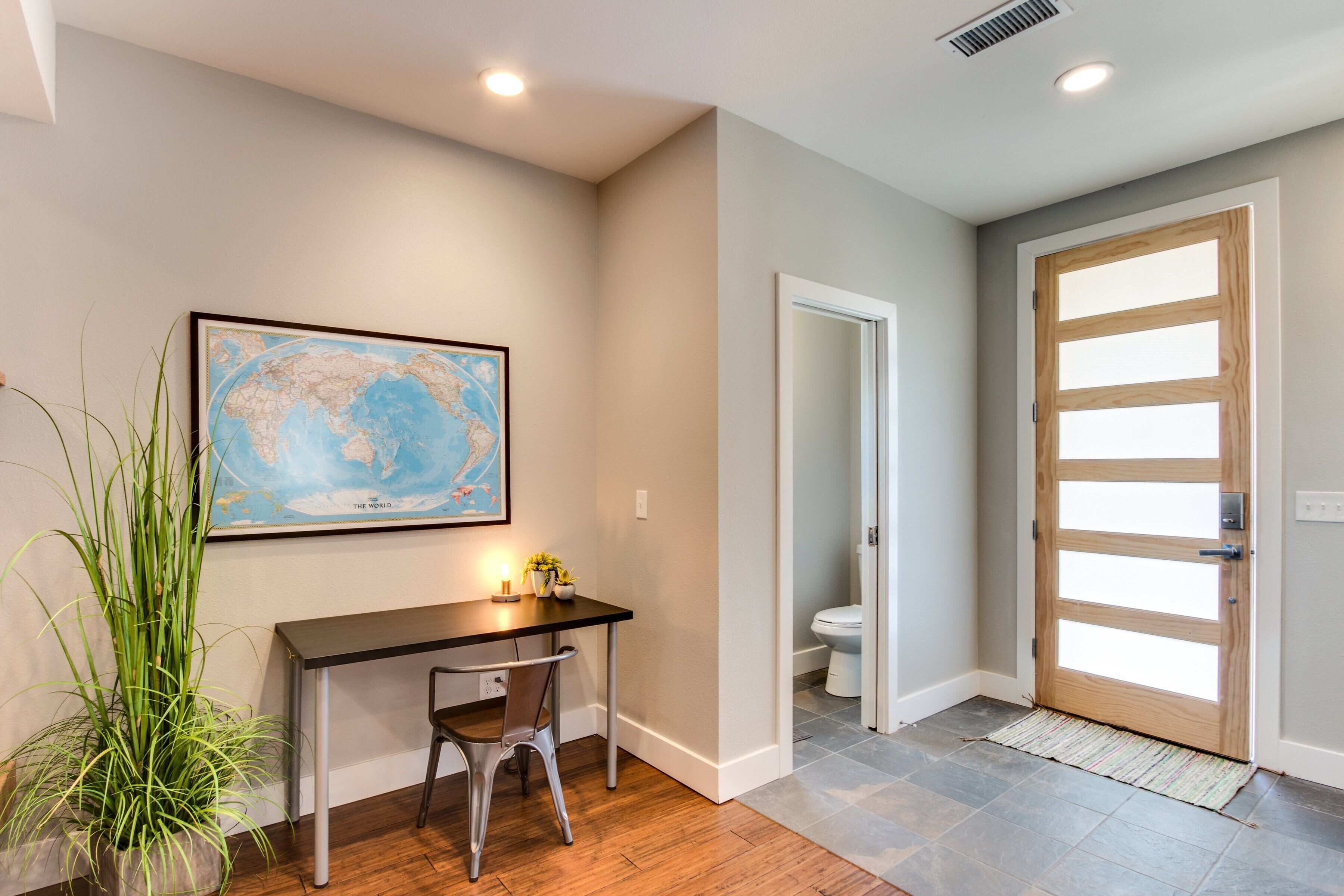 A room with a desk, chair, a world map on the wall, a potted plant, and a wooden door.