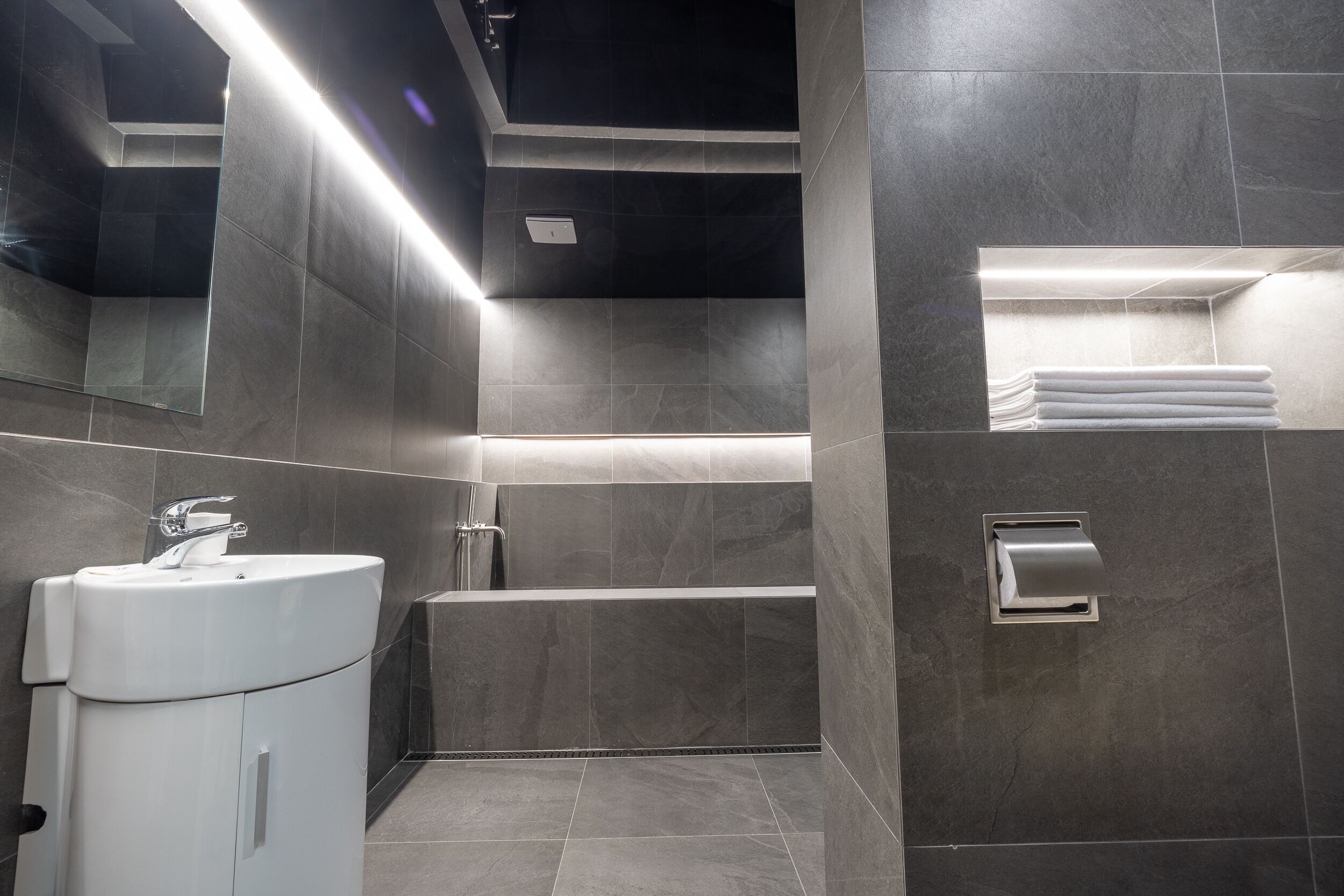 A modern bathroom with a white sink, a mirror, a towel rack, and a built-in shower.