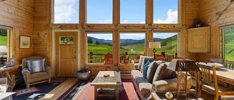 Interno di una baita in legno con un'ampia finestra che si affaccia su un paesaggio verde.