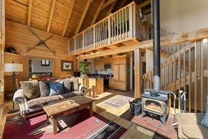 A wooden cabin interior with a loft, kitchen, and a fireplace. - Bear Vista (Crested Butte)