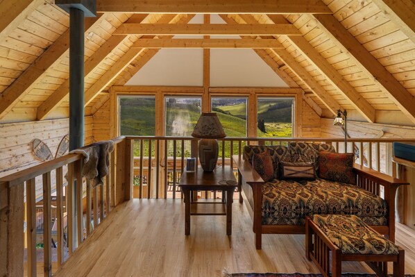 A wooden interior with a high ceiling, a wooden table, a sofa, and a view of a green landscape through large windows. - Bear Vista (Crested Butte)