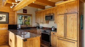 Una cucina con mobili in legno, piani di lavoro in granito, elettrodomestici in acciaio inossidabile e una finestra con vista sul verde.