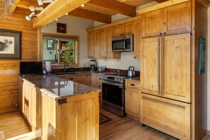 A kitchen with wooden cabinets, granite countertops, stainless steel appliances, and a window overlooking greenery.