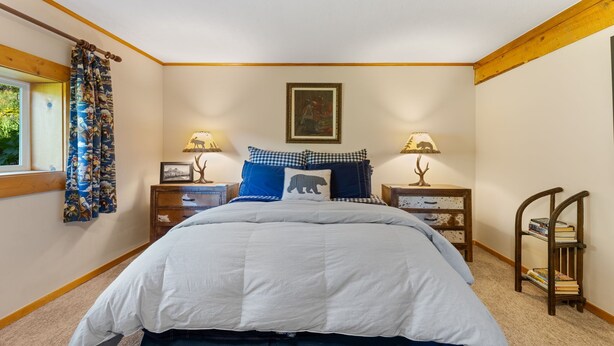 Una camera da letto con un letto grande, due comodini con lampade, una finestra con tende, un quadro al muro e una piccola sedia di legno con libri.