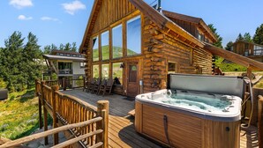 Una baita di legno con idromassaggio, sedie da terrazza e vista sulla foresta circostante.