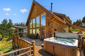 A log cabin with a hot tub, deck chairs, and a view of the surrounding forest.