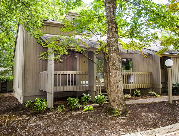 A wooden house with a balcony, a small porch, and a tree in front.
