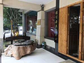 A traditional wooden entrance with a signboard, a stone table with a bench, and a view of the street outside.