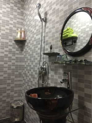 A bathroom with a black sink, a handheld showerhead, a mirror, and a shelf with toiletries.