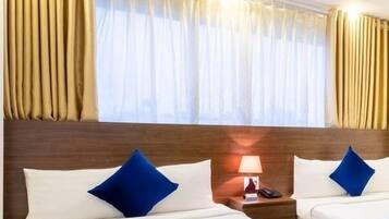 Ein Hotelzimmer mit zwei Betten, jeweils mit weißer und blauer Bettwäsche, einem Holz-Kopfteil, einem Nachttisch mit Lampe und Vorhängen.