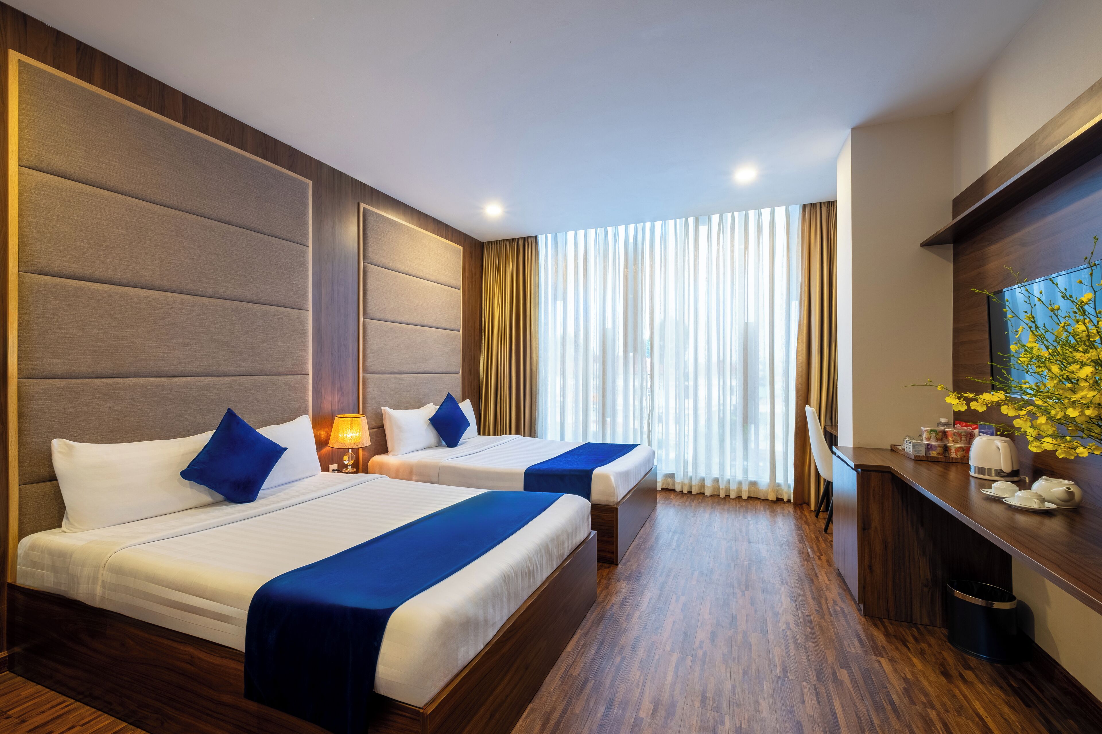 A hotel room with two beds, a desk, a TV, and a window with curtains.
