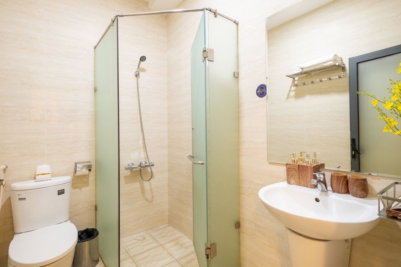 Un bagno moderno con cabina doccia in vetro, un lavandino bianco con accessori in legno e un water con etichetta a marchio visibile.