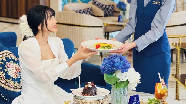 Un vestíbulo de hotel con una mesa de recepción, una zona de estar con un sofá y un jarrón decorativo con flores.