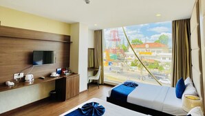 Habitación de hotel con dos camas, un escritorio, un televisor y una ventana con vistas a la ciudad.