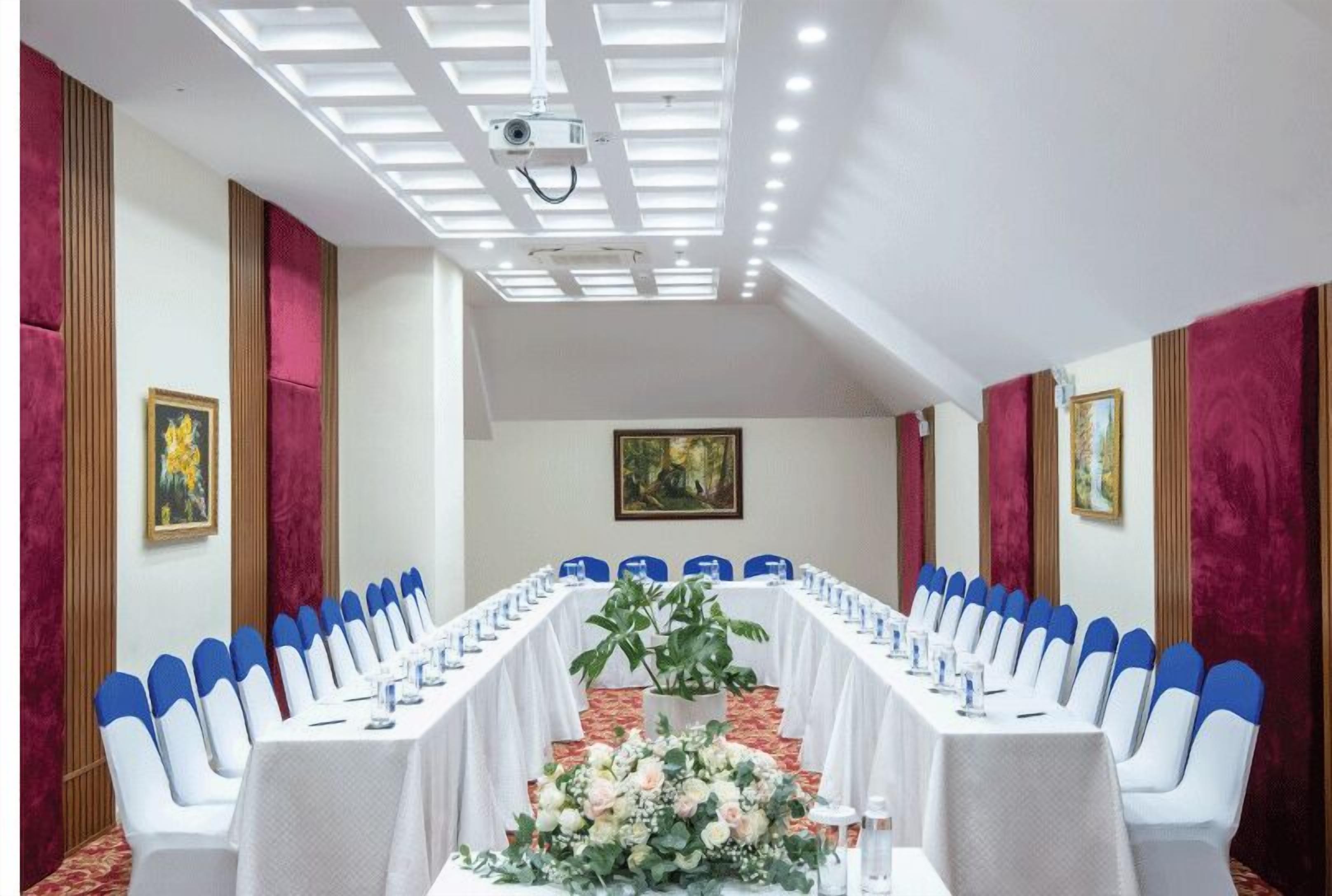 A conference room with a long table, blue chairs, white tablecloths, and floral centerpieces.