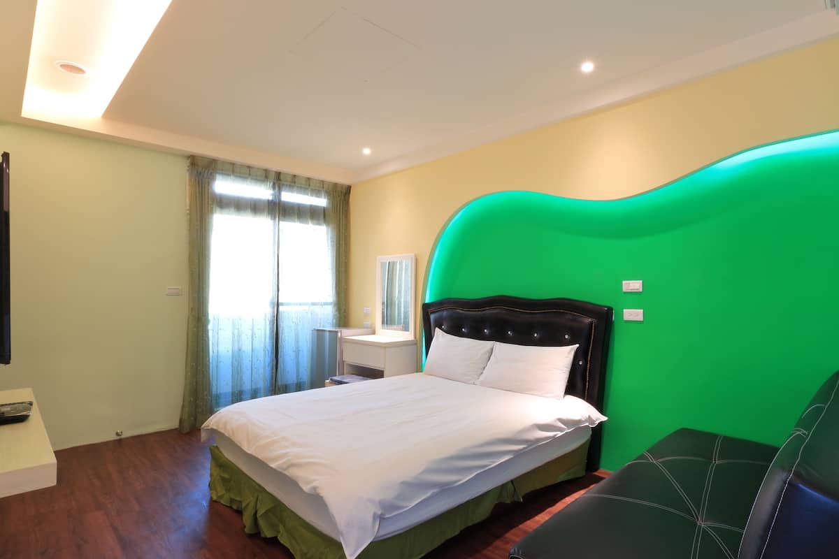 Ein Hotelzimmer mit Bett, Nachttisch, einer grünen Akzentwand und einem Fenster mit Vorhängen.