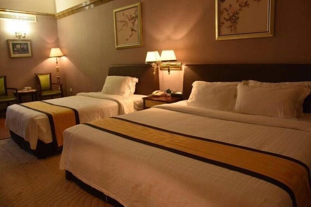 A hotel room with two beds, a nightstand with a lamp, and framed artwork on the walls.