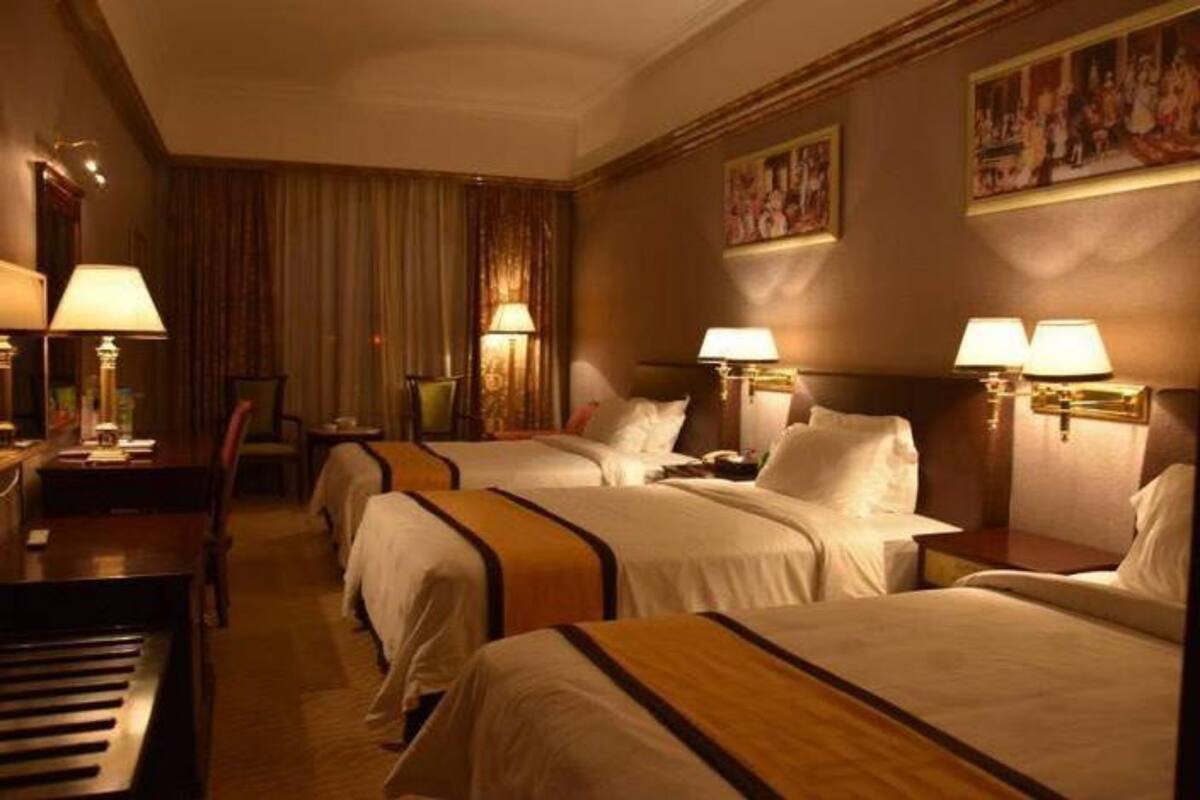 A hotel room with three beds, a piano, and lamps on the walls.