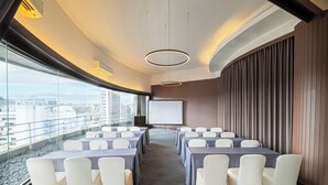 A conference room with tables and chairs, a projector screen, and a view of the city through large windows. - Just Sleep Taipei NTU (Taipei)