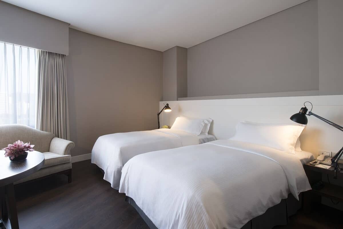 A hotel room with two beds, a desk, a chair, and a window with curtains.