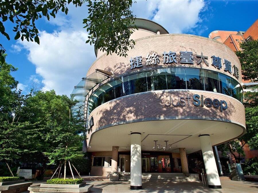 A modern building with a curved facade, large glass windows, and a sign reading "Just Sleep".