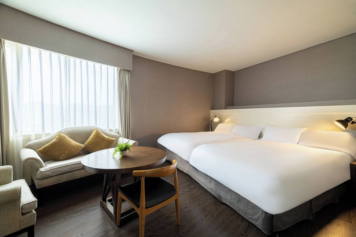 A hotel room with a large bed, a sofa, a round table, and a chair.