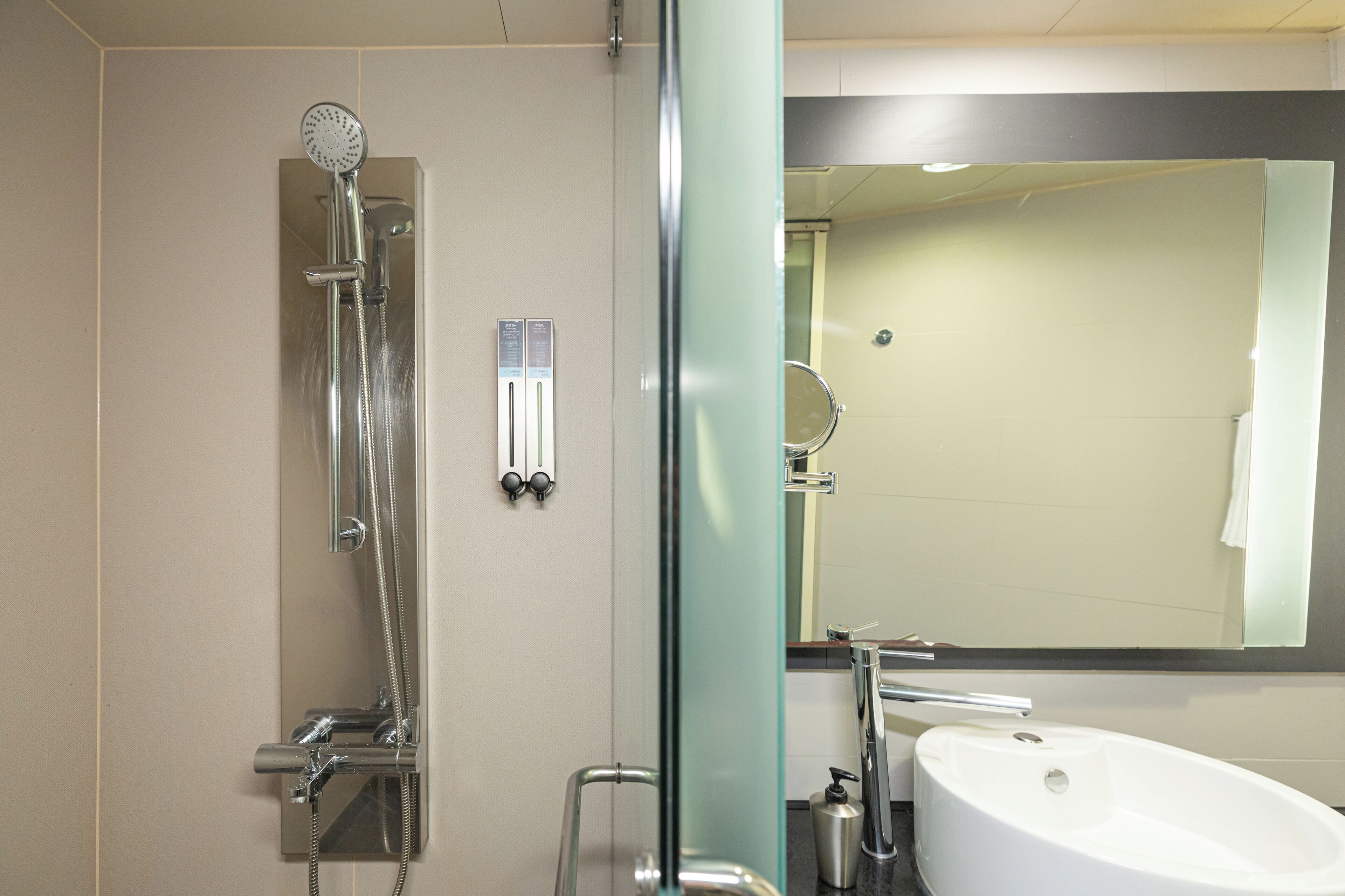 Een moderne badkamer met een douchecabine van glas, een witte wastafel en een spiegel boven de wastafel.