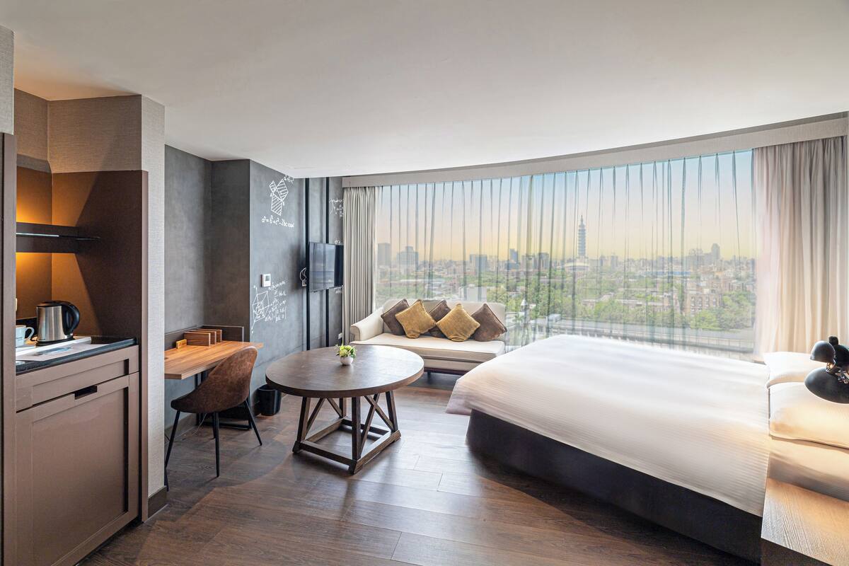 A hotel room with a city view, a dining area, and a bed.