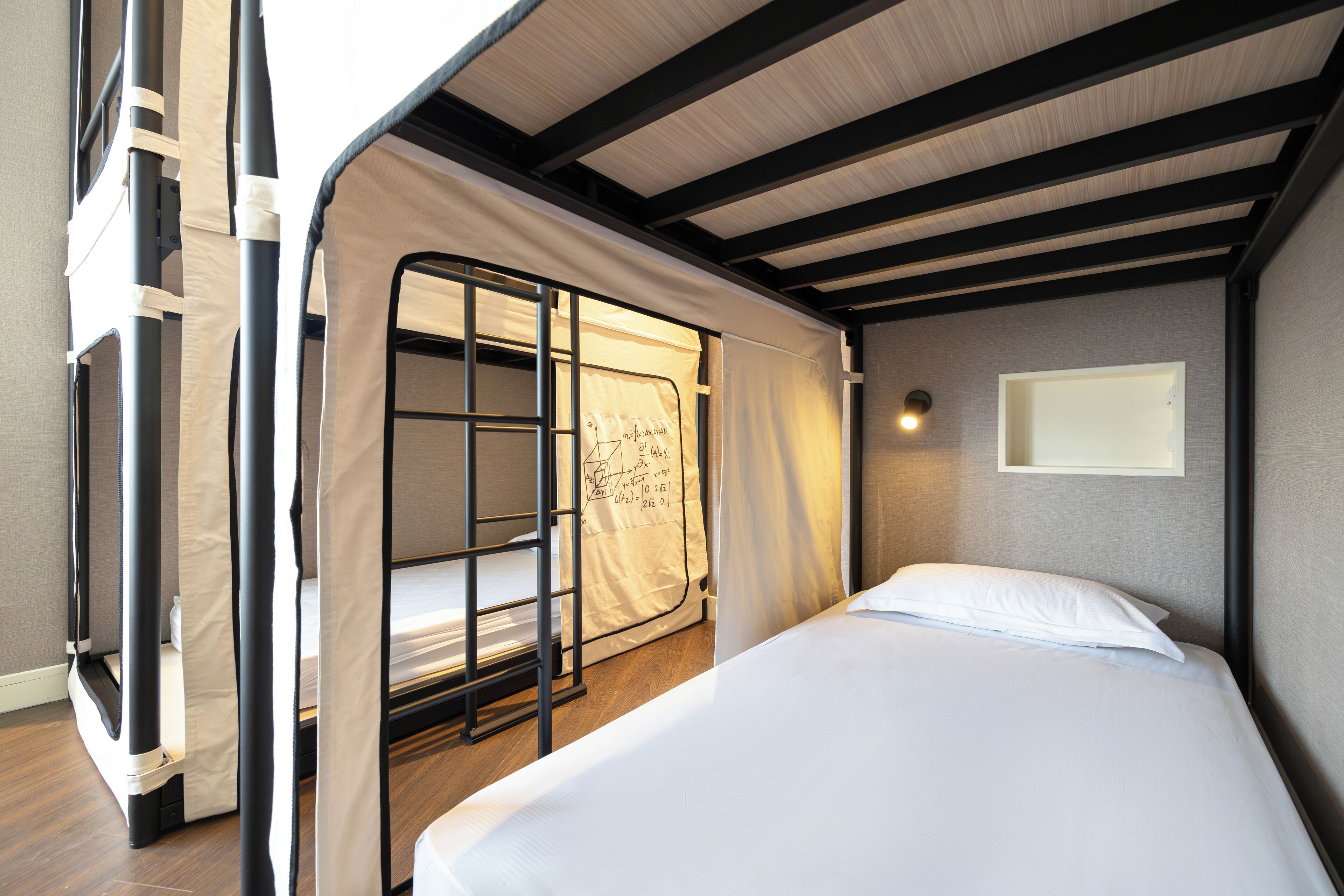 Una cama litera con escalera, una cama individual con almohada y una lámpara fijada a la pared.