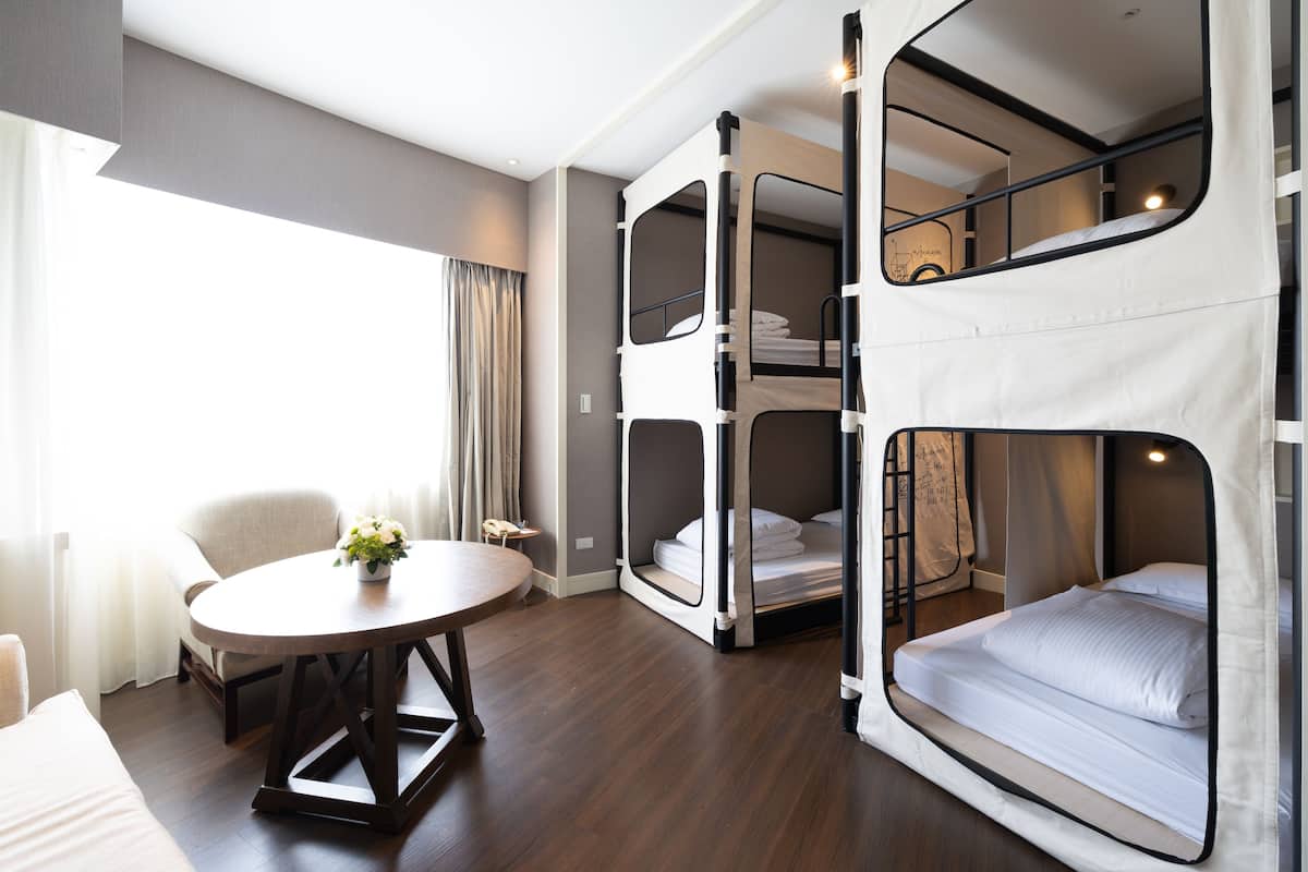 A room with a bunk bed, a round table with a plant, and a chair.