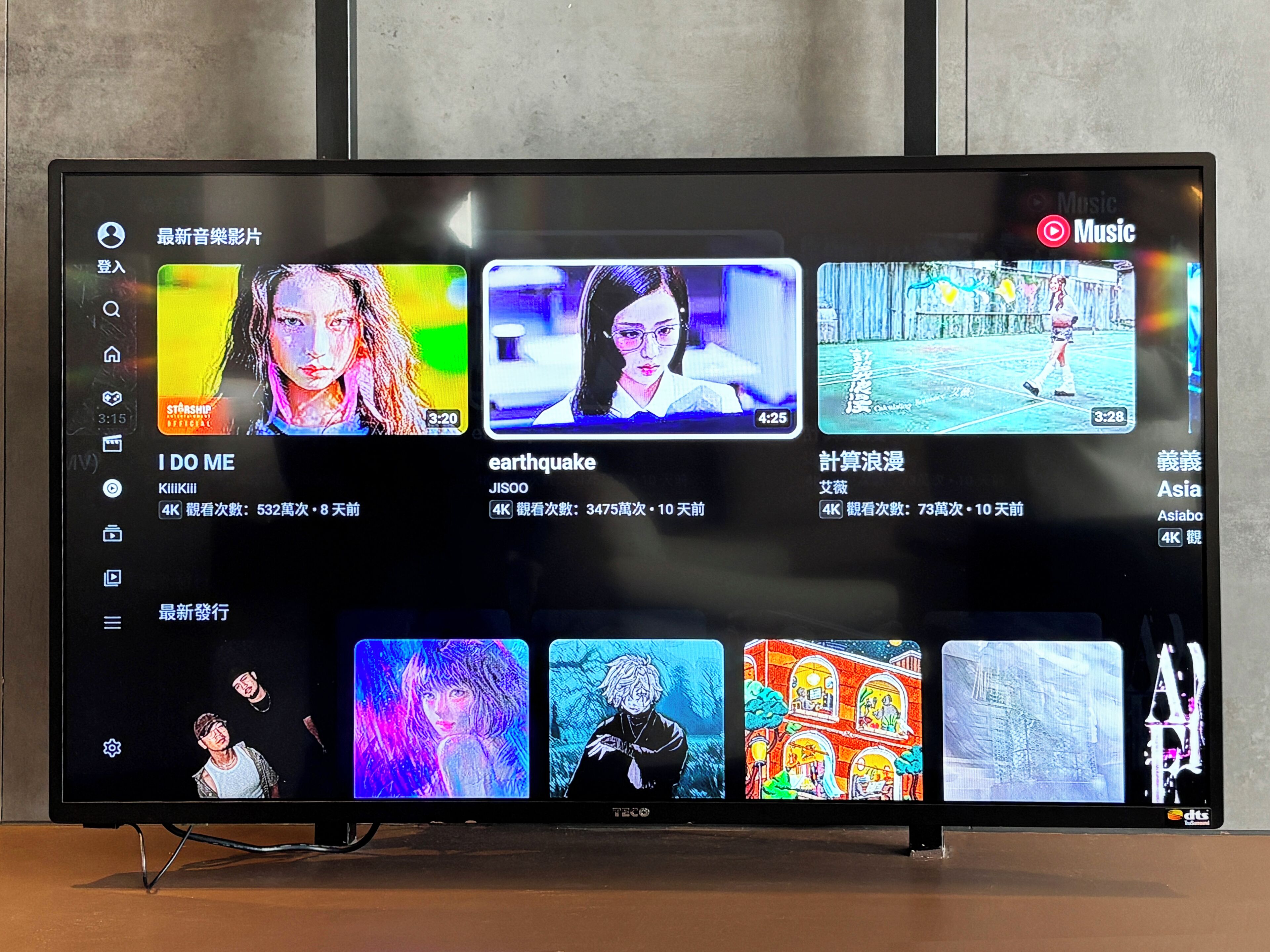 Ein Flachbildfernseher zeigt eine Musikvideo-Player-Oberfläche mit verschiedenen Musikvideos und deren Wiedergabezahlen.