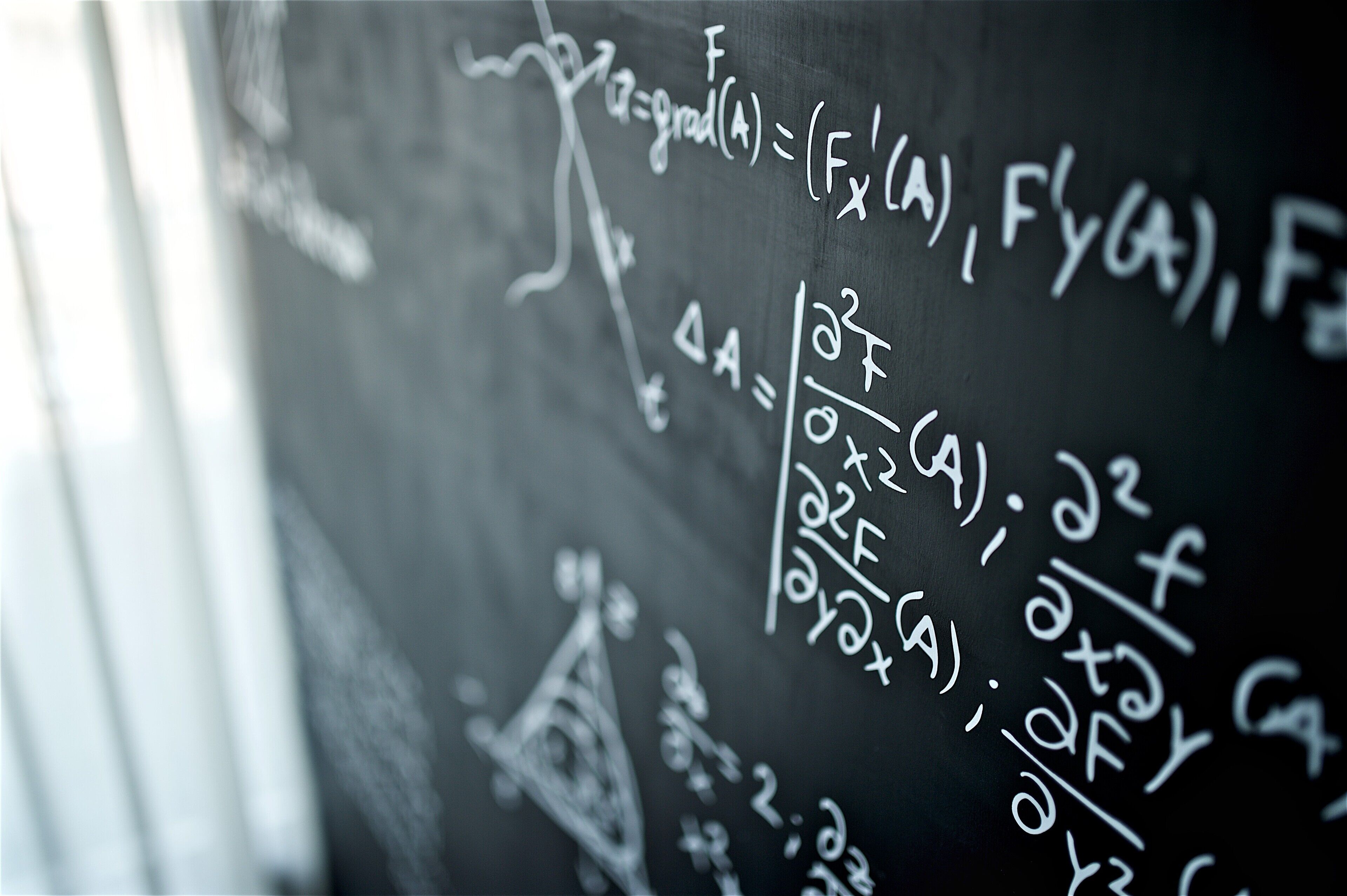 A close-up of a blackboard with mathematical equations and symbols.