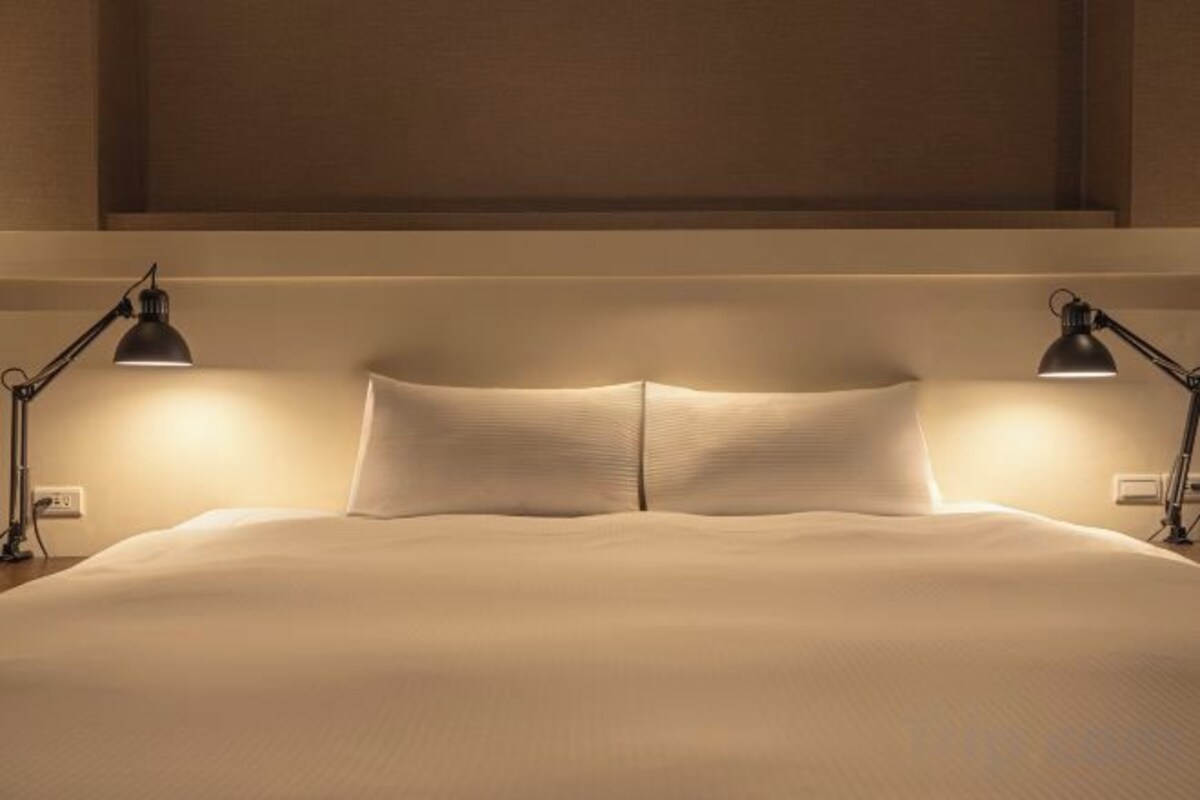 A neatly made bed with two bedside lamps, a headboard, and a wall-mounted light fixture.