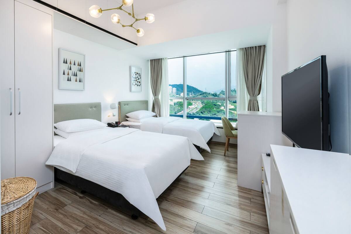Ein modernes Hotelzimmer mit zwei Betten, einem großen Fenster mit Blick auf die Stadt, einem Flachbildfernseher und Holzboden.